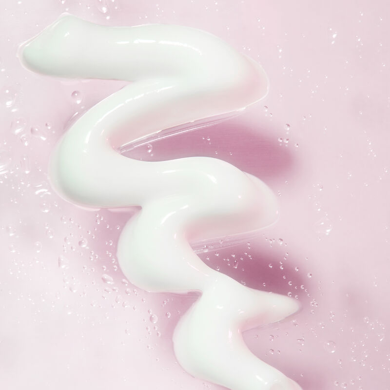 Frottis de l&rsquo;Hydratant Mary Kay parmi des gouttelettes d&rsquo;eau sur un fond rose p&acirc;le