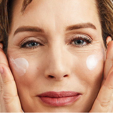 Woman smiling at the camera while applying Mary Kay TimeWise Replenishing Serum C+E on both cheeks