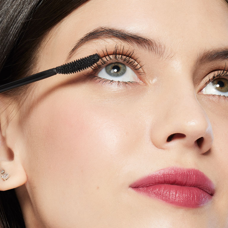 Model holding Mary Kay Great Heights Mascara applicator up to her eye